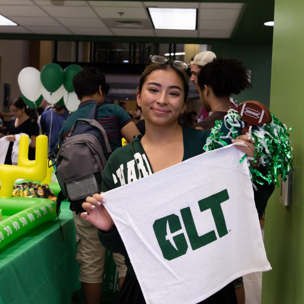 Smiling student with Charlotte sweatshirt poses with CLT rally towel in Charlotte Barnes & Noble