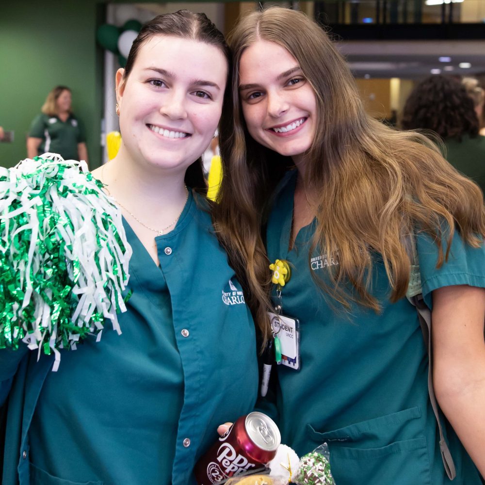 Two nursing students smile with a green and white pom pom and drinks and snacks from College Colors Day